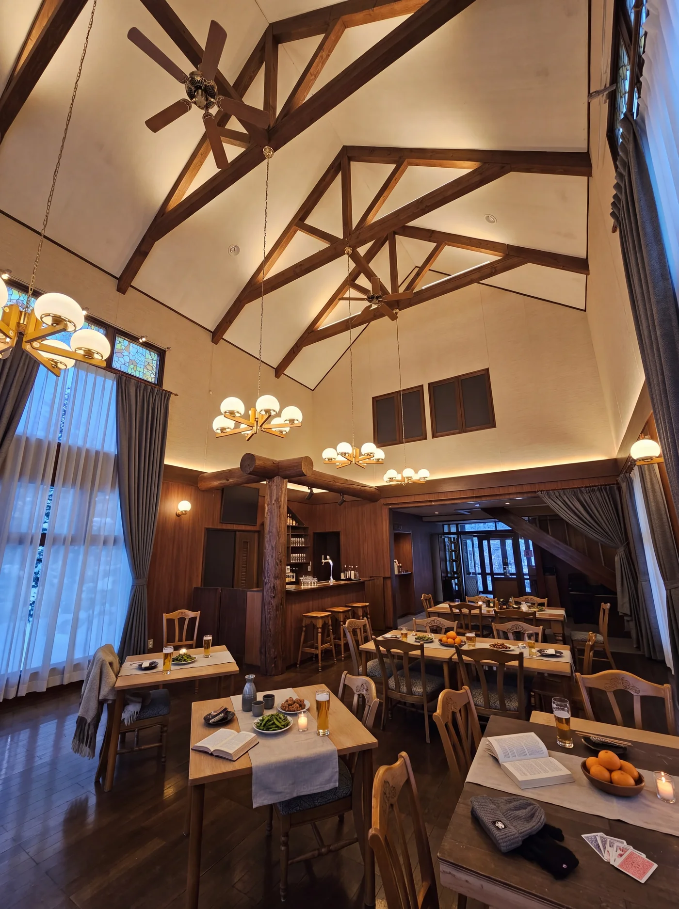 The dining room and bar at dusk: globe chandeliers under the trusses, beers and snacks on the tables