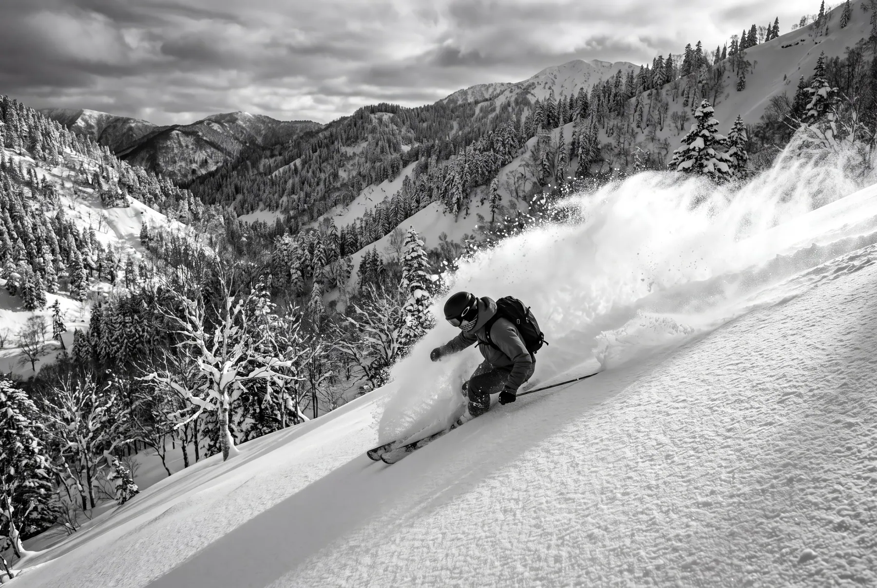 A skier making a deep powder turn on an open face above a forested valley