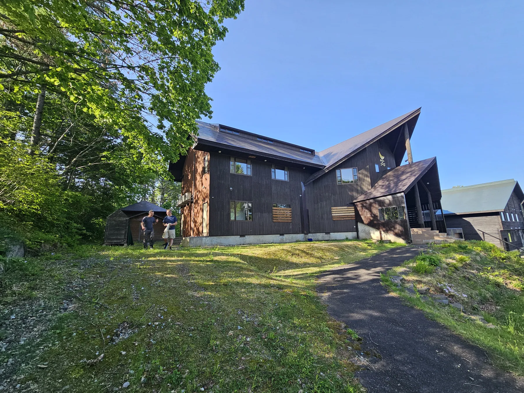 The lodge in summer: dark timber, steep roofs, deep green trees and a grass approach